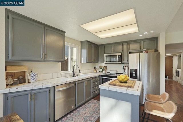 kitchen featuring appliances with stainless steel finishes, tile countertops, dark hardwood / wood-style floors, and sink