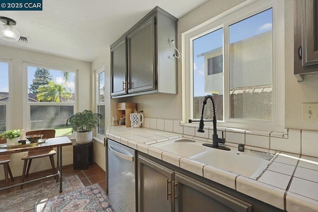 kitchen with tile counters, stainless steel dishwasher, plenty of natural light, and dark tile patterned floors