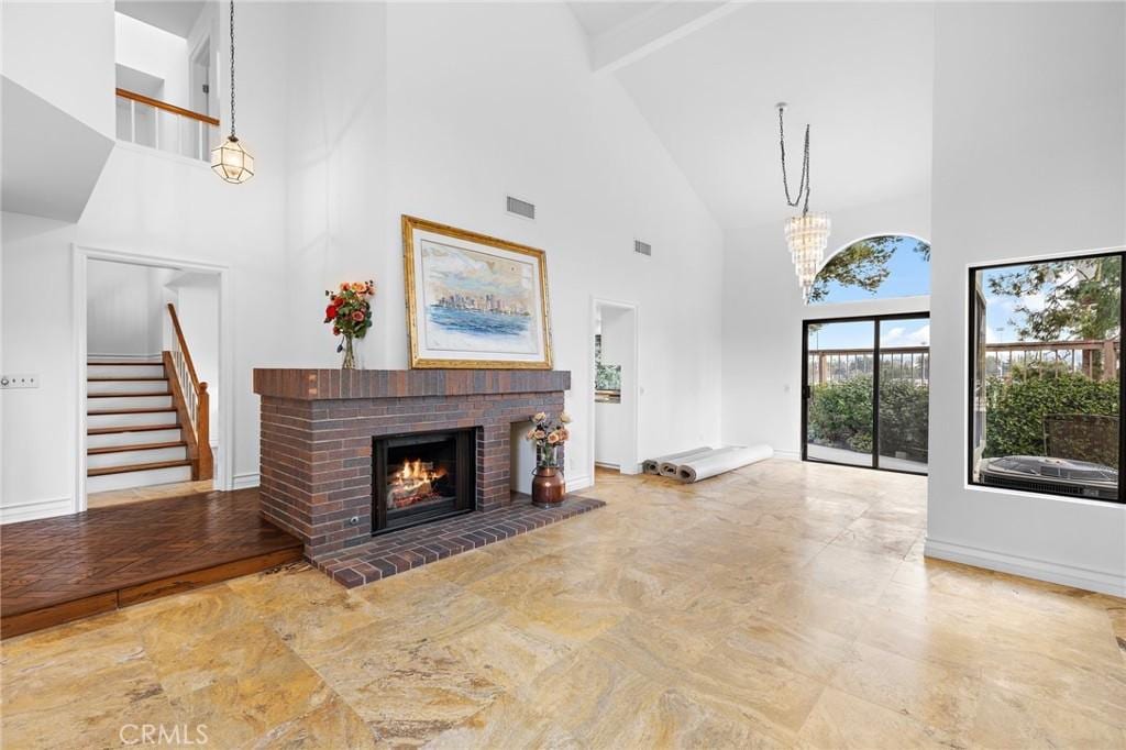 living room with an inviting chandelier, a fireplace, beamed ceiling, and a high ceiling