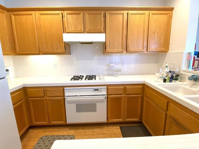 kitchen with tile counters, sink, backsplash, and white appliances