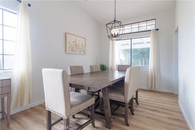 dining space with vaulted ceiling, an inviting chandelier, and light hardwood / wood-style flooring