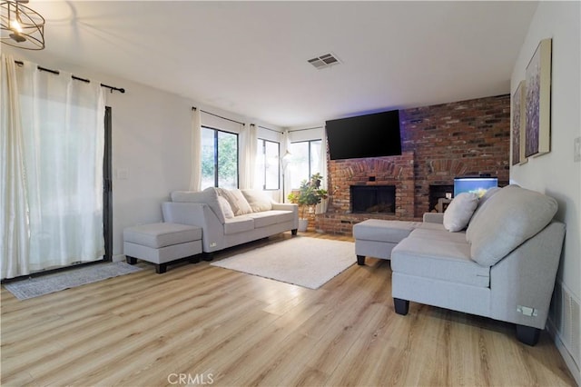 living room featuring a brick fireplace, an inviting chandelier, and light hardwood / wood-style flooring