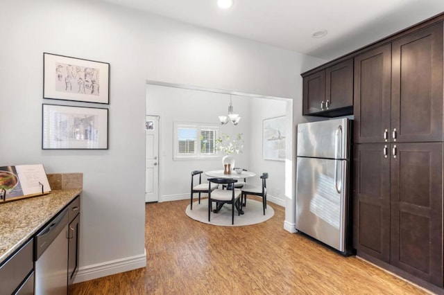 kitchen featuring light stone countertops, appliances with stainless steel finishes, a chandelier, light wood-type flooring, and dark brown cabinets