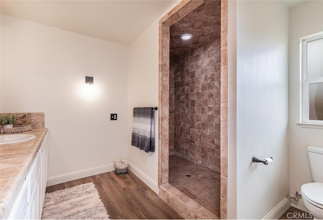 bathroom with toilet, hardwood / wood-style floors, tiled shower, and vanity