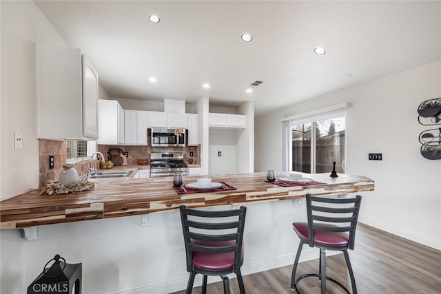 kitchen featuring wooden counters, kitchen peninsula, sink, appliances with stainless steel finishes, and white cabinets