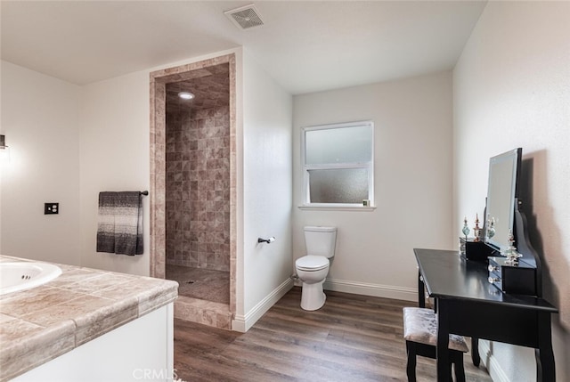 bathroom with hardwood / wood-style floors, toilet, vanity, and a tile shower