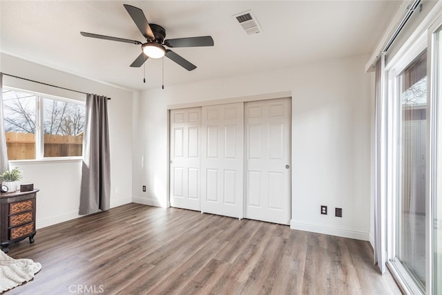 unfurnished bedroom with ceiling fan, a closet, multiple windows, and wood-type flooring