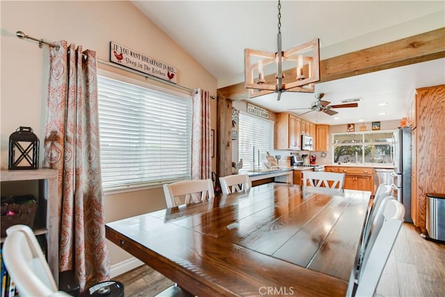 dining area featuring ceiling fan with notable chandelier, vaulted ceiling, and light wood-type flooring