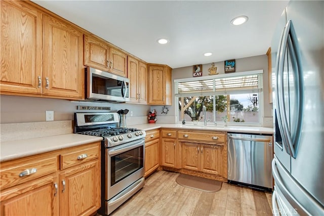 kitchen with appliances with stainless steel finishes, sink, and light hardwood / wood-style flooring