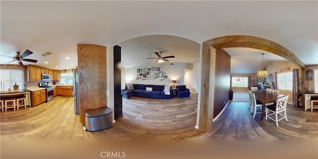 interior space featuring ceiling fan with notable chandelier, hanging light fixtures, appliances with stainless steel finishes, and light hardwood / wood-style flooring