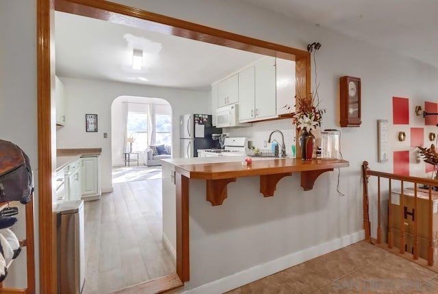 kitchen with white appliances, white cabinetry, sink, kitchen peninsula, and a breakfast bar area