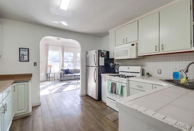 kitchen with tile counters, white appliances, light wood-type flooring, white cabinets, and sink