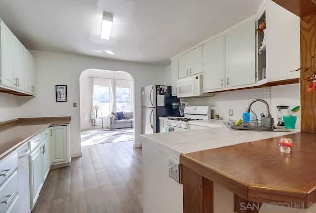 kitchen with white appliances, white cabinets, backsplash, kitchen peninsula, and light hardwood / wood-style flooring