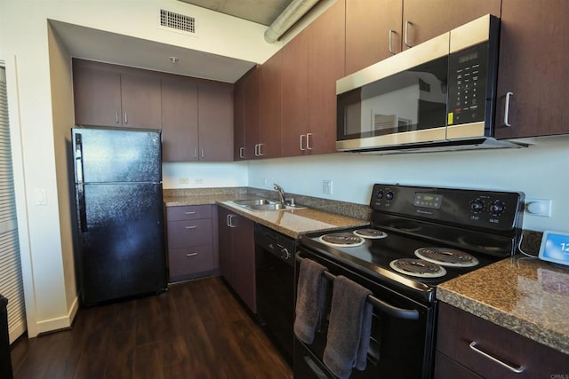 kitchen with dark stone countertops, black appliances, sink, dark brown cabinetry, and dark wood-type flooring