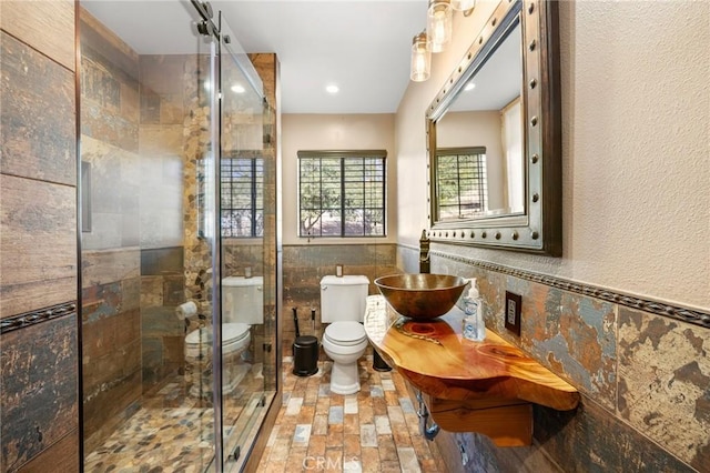 bathroom with a wainscoted wall, a sink, a shower stall, tile walls, and toilet