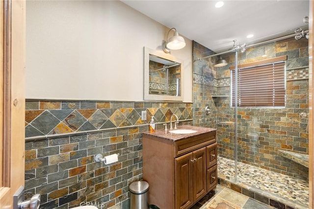 bathroom featuring a shower stall, vanity, wainscoting, stone finish floor, and tile walls