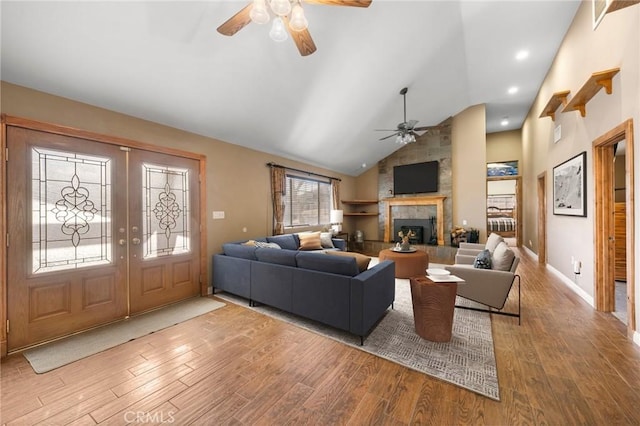 living area with vaulted ceiling, a tile fireplace, french doors, wood finished floors, and a ceiling fan