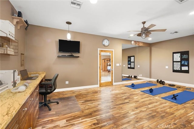 exercise room with ceiling fan, visible vents, baseboards, and wood finished floors