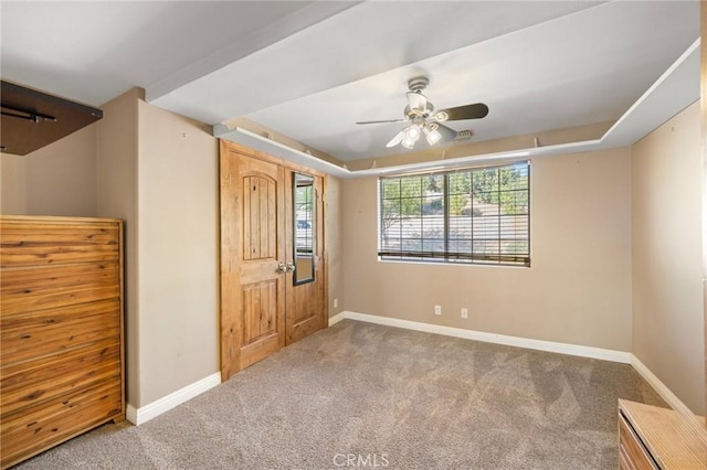 carpeted entryway featuring a tray ceiling, baseboards, and a ceiling fan