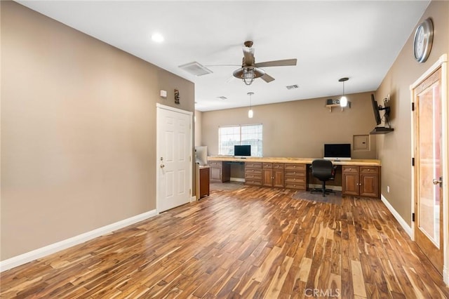 unfurnished office featuring built in desk, a ceiling fan, baseboards, and wood finished floors