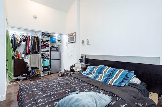 bedroom with a wall unit AC, hardwood / wood-style flooring, and stainless steel fridge