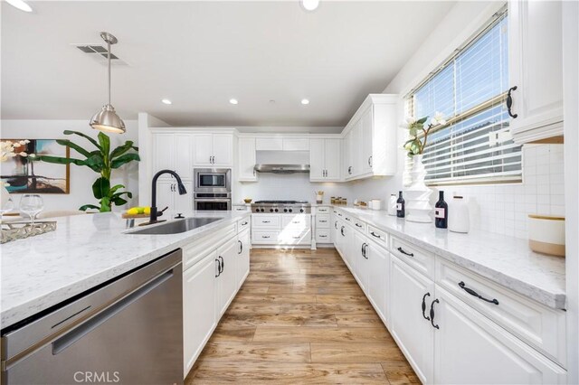 kitchen with sink, hanging light fixtures, light stone countertops, appliances with stainless steel finishes, and white cabinets