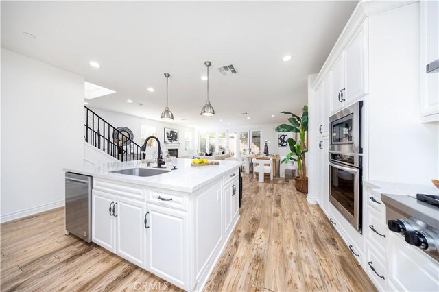 kitchen with a kitchen island with sink, sink, stainless steel appliances, and white cabinetry