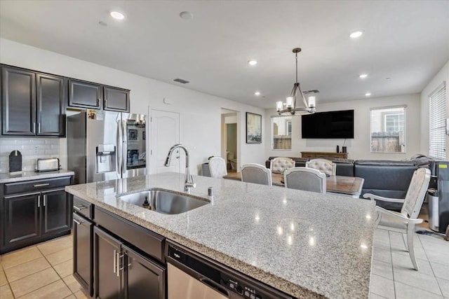 kitchen with stainless steel appliances, an island with sink, sink, a chandelier, and light stone counters