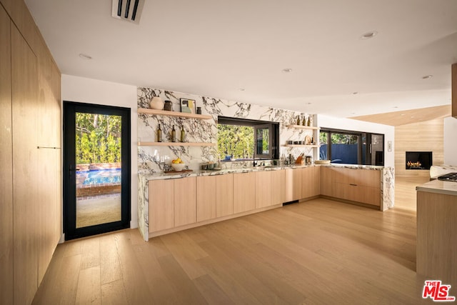 kitchen with light brown cabinetry, a wealth of natural light, light hardwood / wood-style flooring, and a fireplace