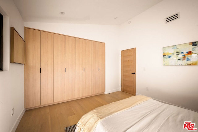 bedroom with light wood-type flooring, vaulted ceiling, and a closet