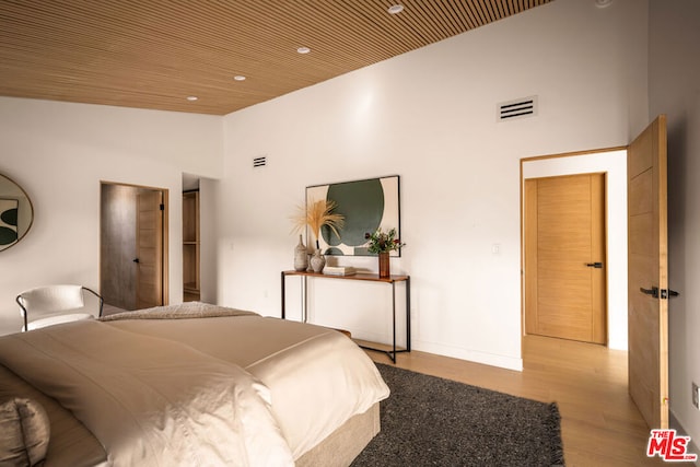 bedroom with wood ceiling, a high ceiling, and light hardwood / wood-style flooring