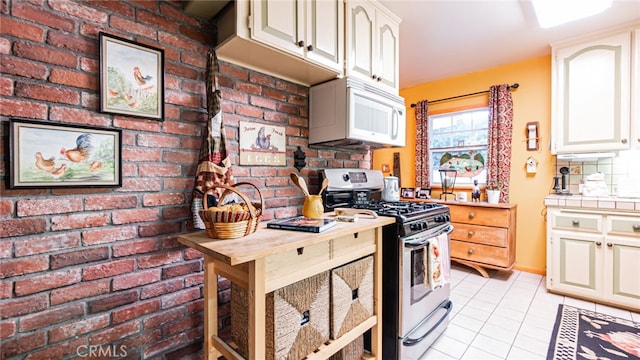 kitchen featuring stainless steel range with gas cooktop, brick wall, and light tile patterned floors