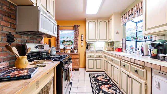 kitchen featuring light tile patterned floors, stainless steel gas range, tile counters, backsplash, and sink