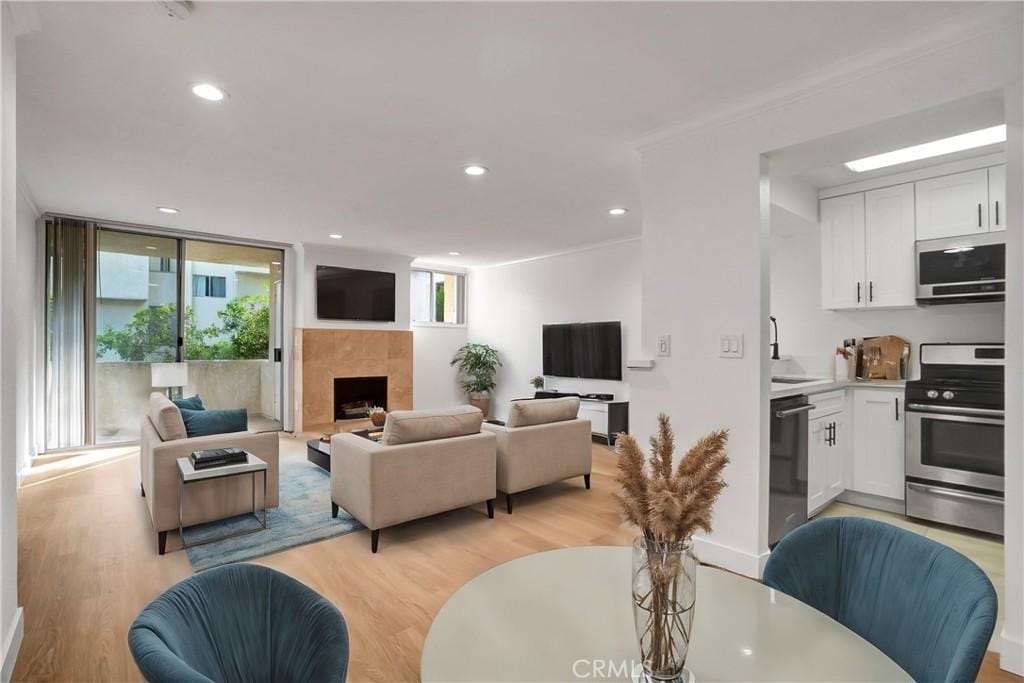 living room with expansive windows, a tiled fireplace, sink, and light wood-type flooring