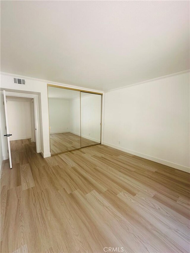 unfurnished bedroom with a closet, crown molding, and light hardwood / wood-style floors