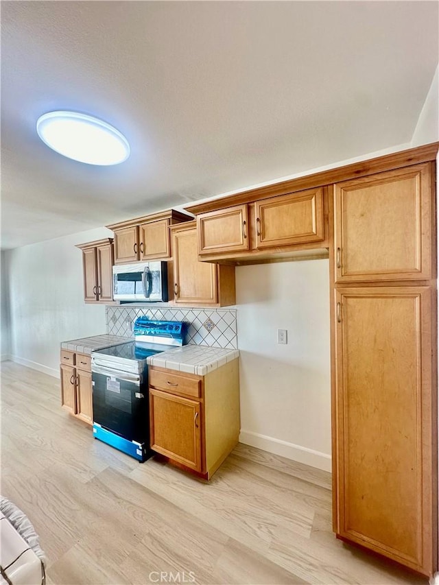 kitchen featuring light wood-type flooring, brown cabinets, backsplash, appliances with stainless steel finishes, and tile counters