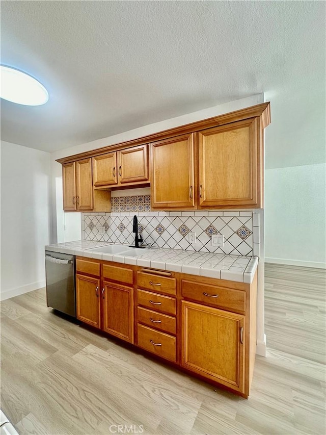 kitchen featuring backsplash, brown cabinets, stainless steel dishwasher, and a sink