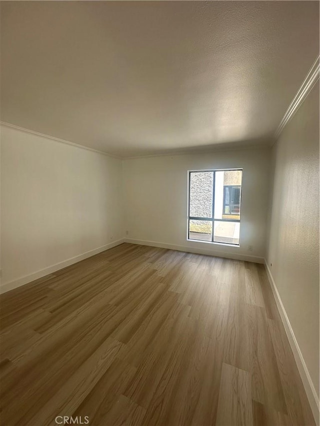 empty room featuring baseboards, wood finished floors, and ornamental molding