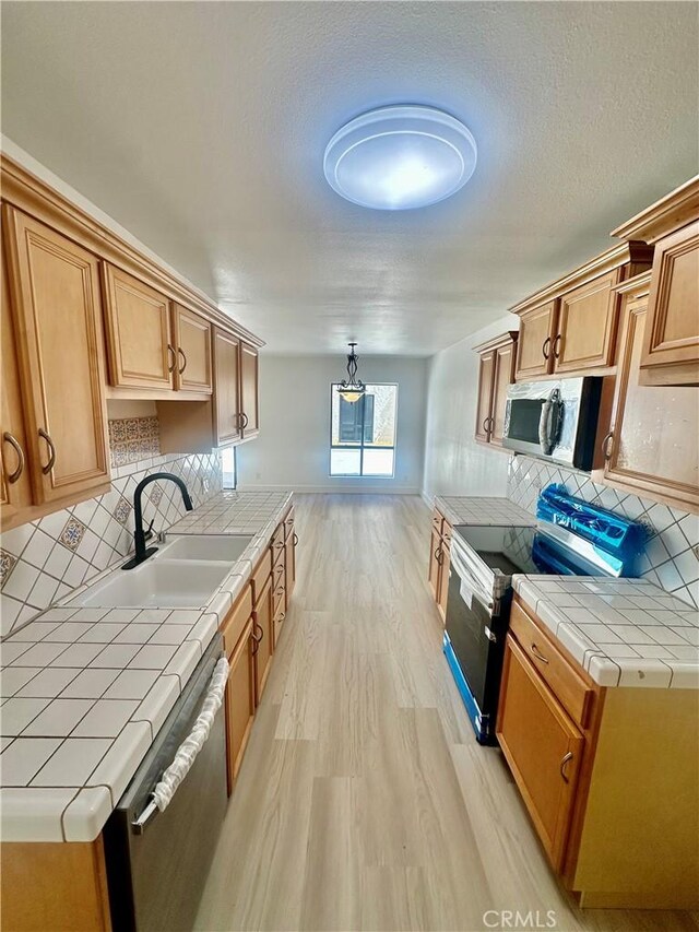 kitchen with appliances with stainless steel finishes, tile counters, sink, backsplash, and light hardwood / wood-style flooring