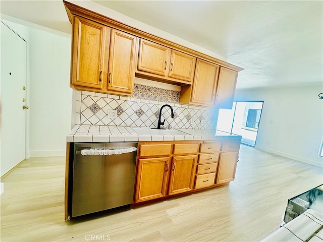 kitchen with dishwasher, light wood finished floors, backsplash, and a sink