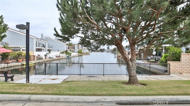 view of home's community with a lawn, a water view, and fence