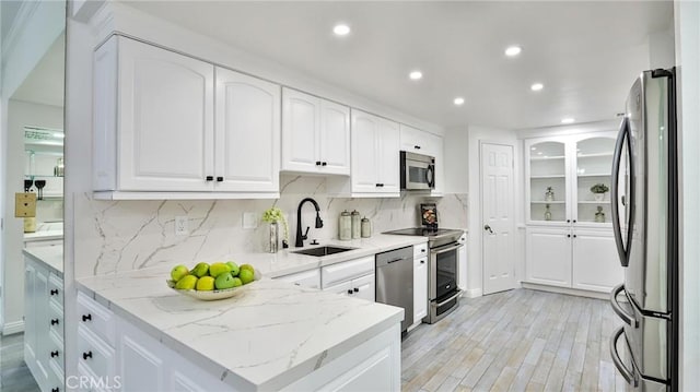 kitchen featuring stainless steel appliances, a sink, white cabinetry, and light stone countertops