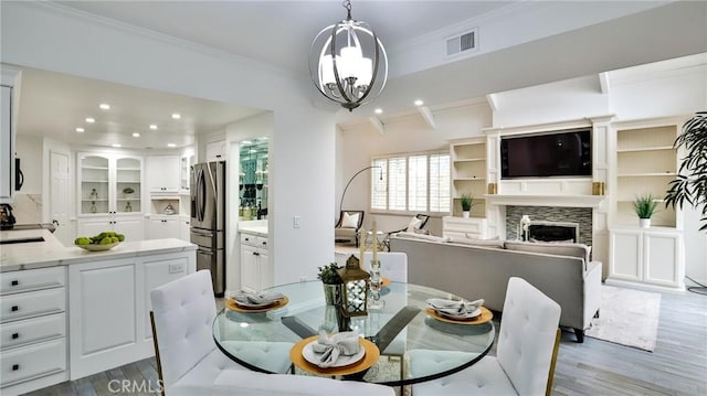 dining room featuring visible vents, a fireplace, light wood-style flooring, and crown molding