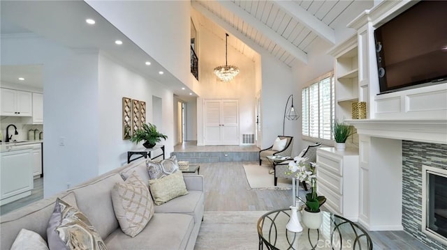 living area featuring beam ceiling, a fireplace, recessed lighting, wood finished floors, and a chandelier