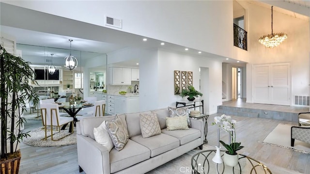 living area featuring visible vents, a notable chandelier, light wood-style flooring, and a towering ceiling