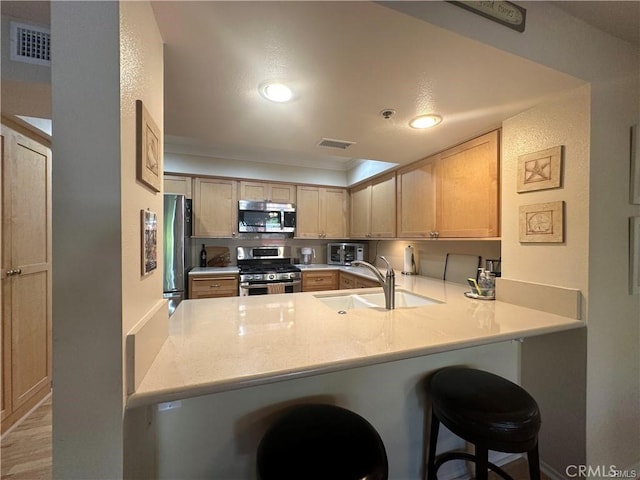 kitchen featuring a kitchen bar, stainless steel appliances, light brown cabinetry, sink, and kitchen peninsula