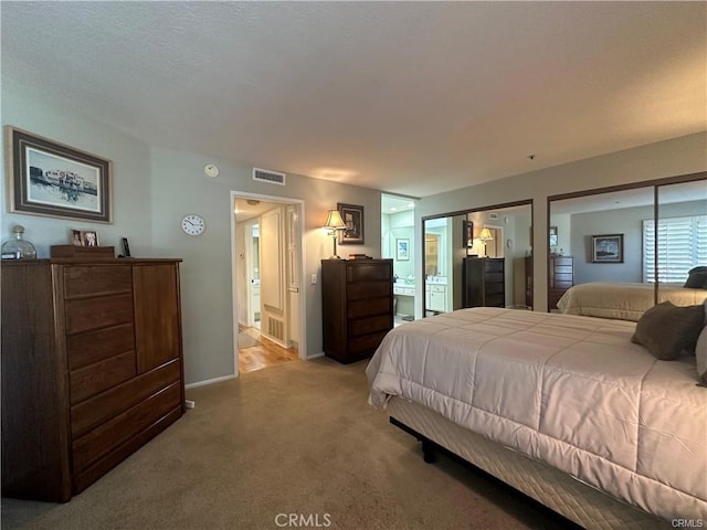 bedroom with two closets, ensuite bath, and light carpet