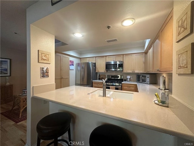 kitchen featuring appliances with stainless steel finishes, light brown cabinets, ornamental molding, kitchen peninsula, and a breakfast bar area