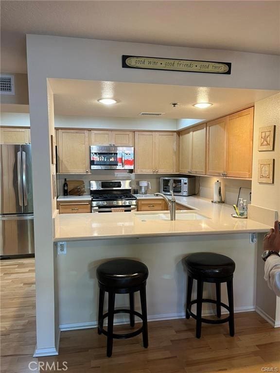 kitchen with a breakfast bar, light brown cabinetry, and appliances with stainless steel finishes