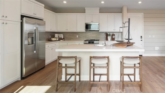 kitchen with a kitchen breakfast bar, stainless steel appliances, white cabinets, and a center island with sink